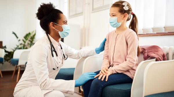 A female physician comforts a child wearing a face mask.