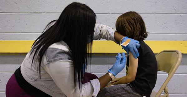 A child is given a COVID-19 vaccine dose by a female healthcare provider.