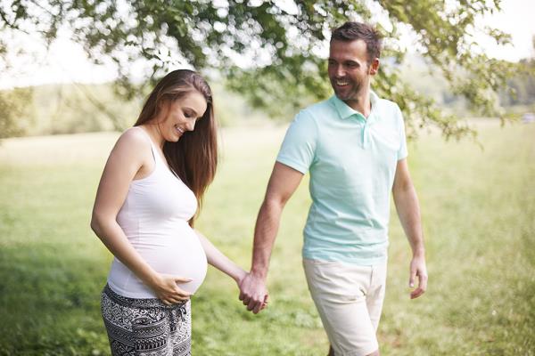 smiling pregnant couple holding hands outside