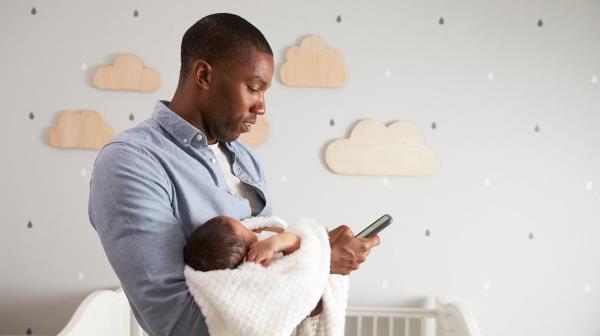 father co<em></em>nsults his phone while holding newborn