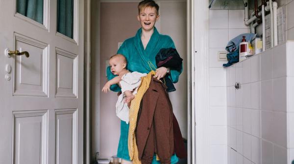 parent in robe has hands full with baby and clothing