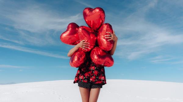 person holding six red, heart-shaped balloons in front of their face