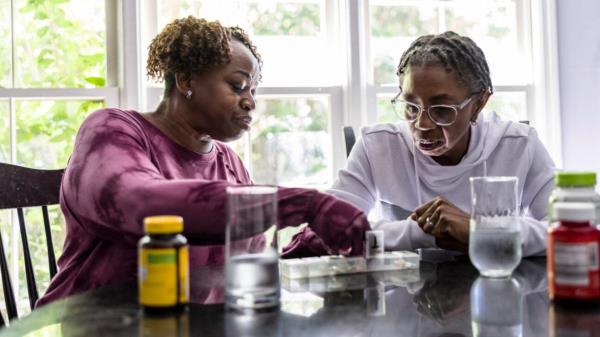 Two older women inspect a tray of pills