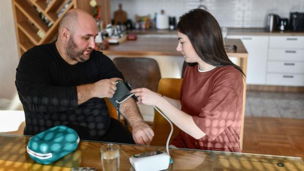A woman helps a man put on a blood pressure cuff.
