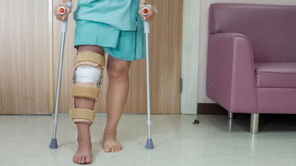 A hosptial patient is seen on crutches with a bandage around their knee