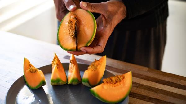 A person cuts cantaloupe into wedges.