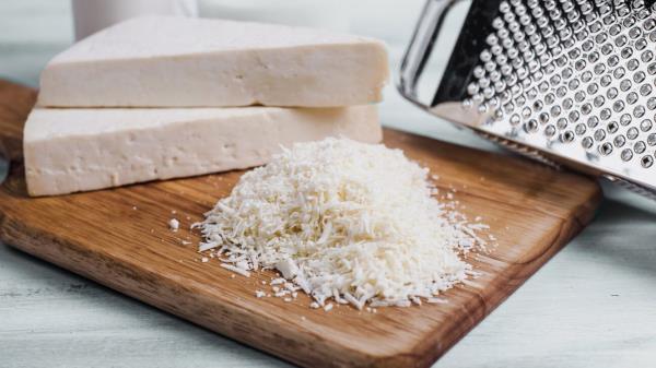 A grated pile of cotiija cheese is seen on a cutting board.