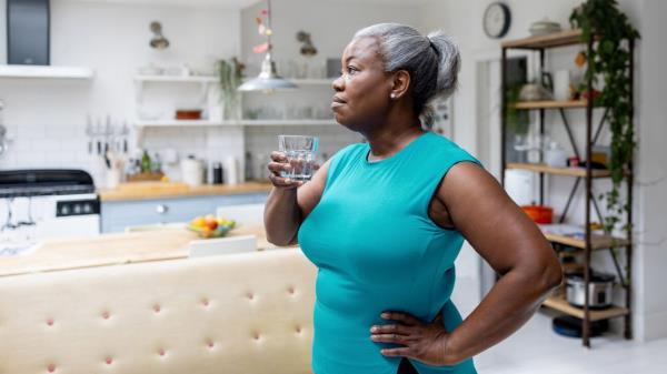 Woman in blue shirt drinks water in a kitchen.