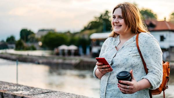 Female holding phone and coffee by a river