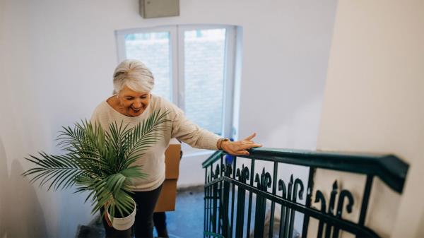 Woman with grey hair walks stairs holding a plant.